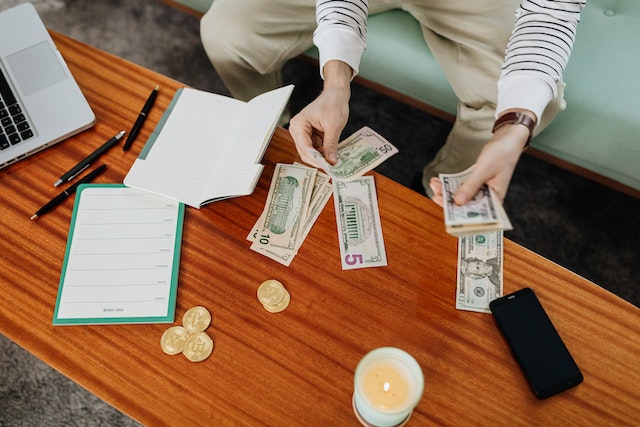 Person handling U.S. dollars over a borwn wooden table